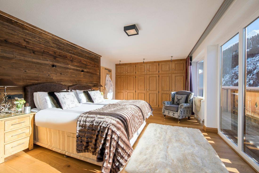 Helles Schlafzimmer mit Holzwand, großem Bett und Zugang zu einem Balkon mit Bergblick.