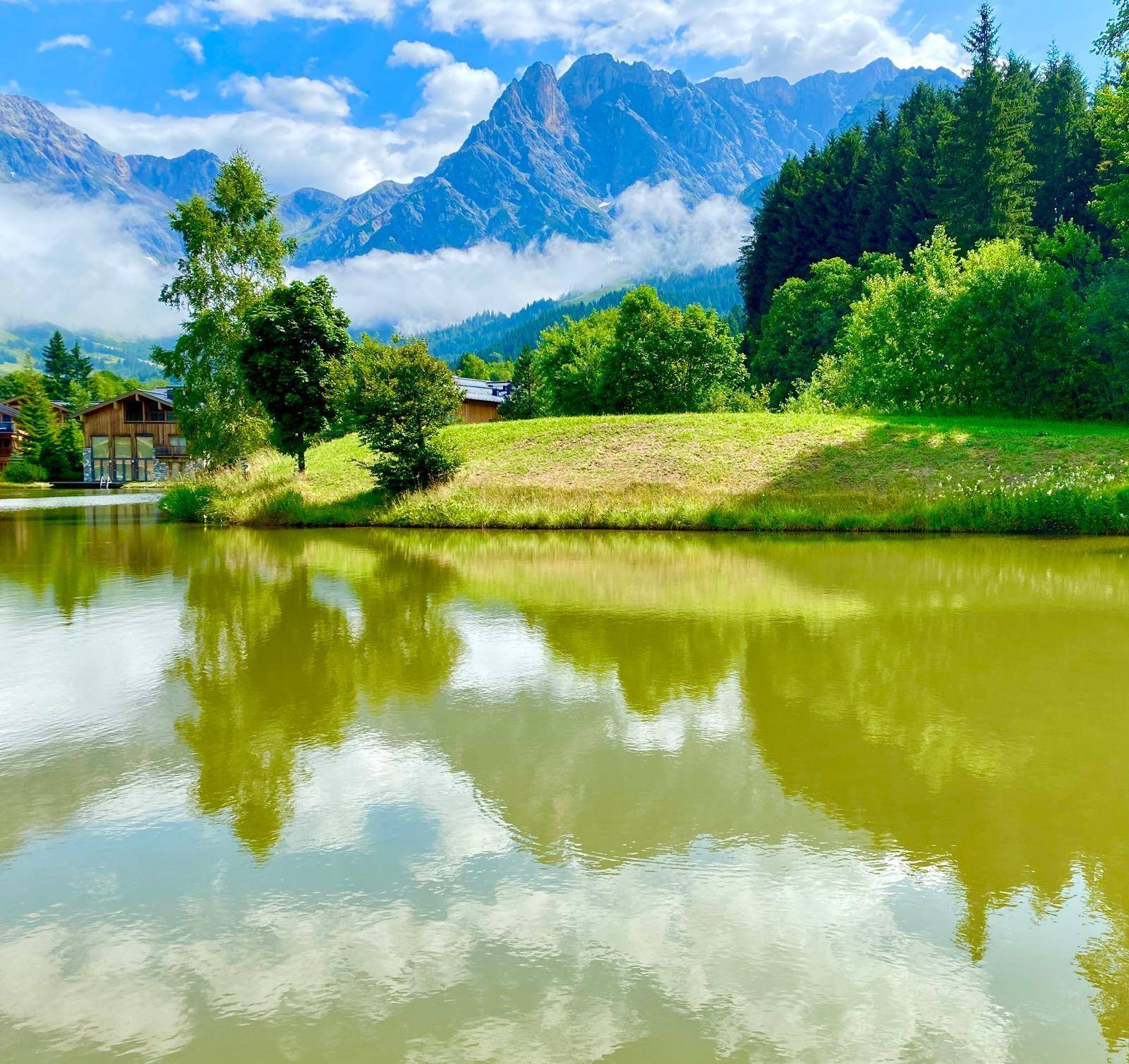 Ruhiger See mit Spiegelungen der Wolken und umliegenden Bergen in einer idyllischen Landschaft.