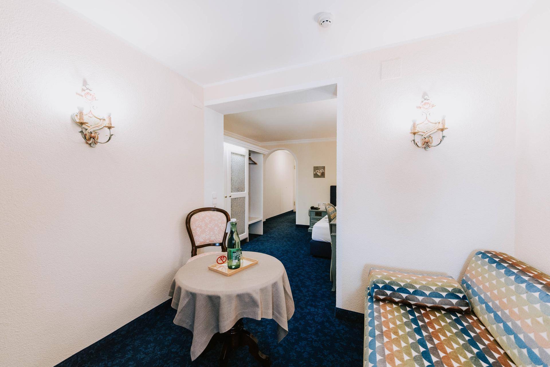 Geräumiges Zimmer mit Teppichboden, kleinem Tisch und Zugang zu einem weiteren Bereich.