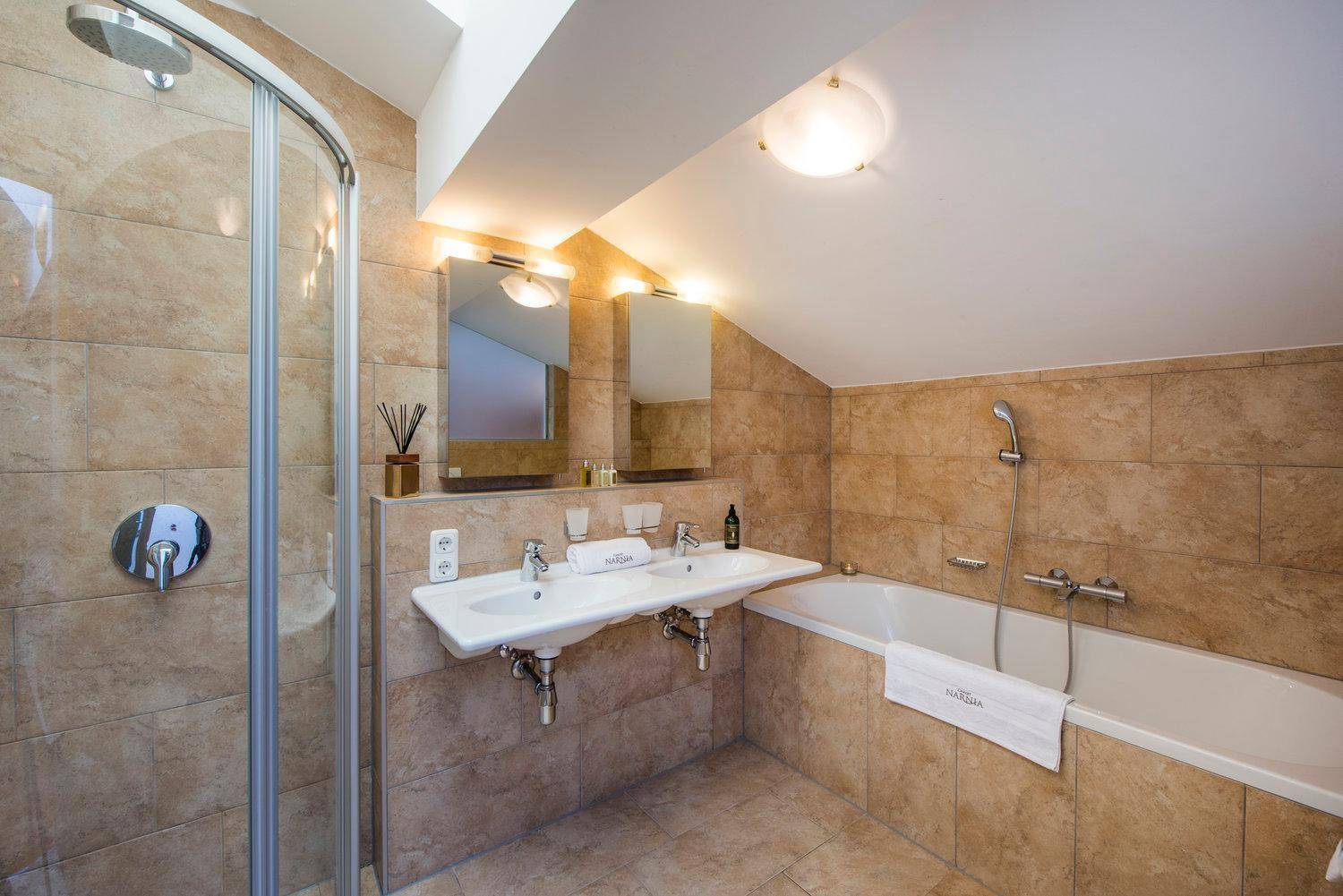 Helles Badezimmer im Dachgeschoss mit Badewanne, Dusche, Doppelwaschbecken und Dachschräge.