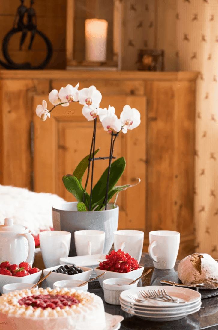 Reich gedeckter Frühstückstisch mit frischen Früchten, Kuchen und Orchideen in traditionellem Ambiente.