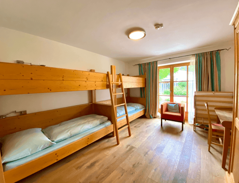Kinderzimmer mit Etagenbetten aus Holz, Holzboden und farbigen Vorhängen für eine fröhliche Atmosphäre.
