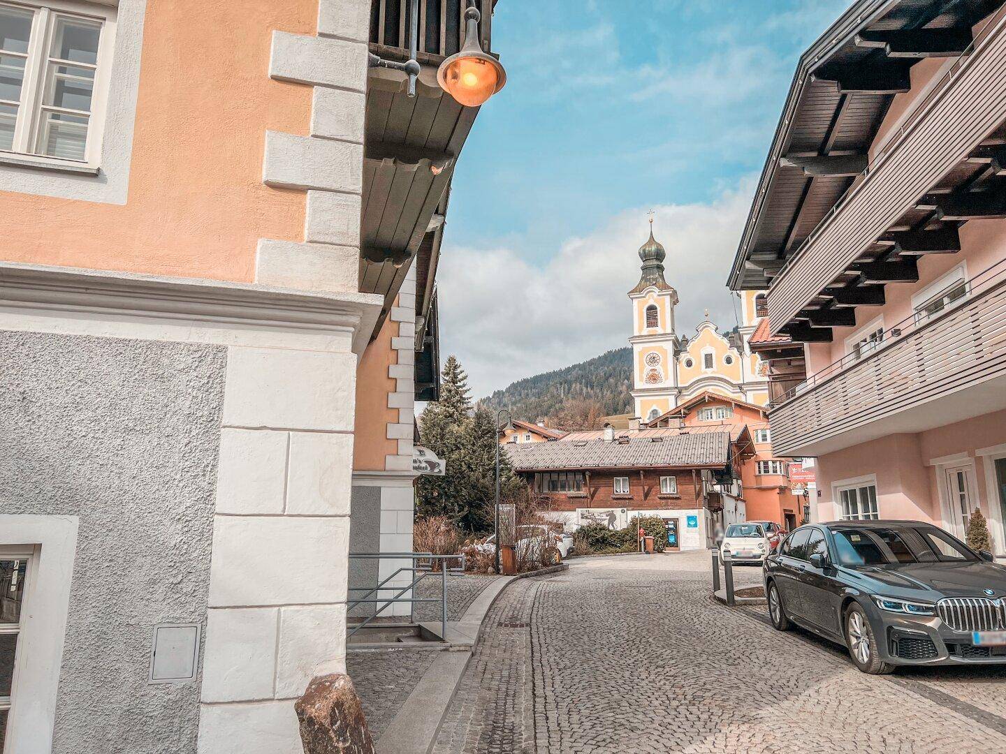 Blick auf eine gepflasterte Straße mit traditionellen Gebäuden und einem markanten Kirchturm im Hintergrund.