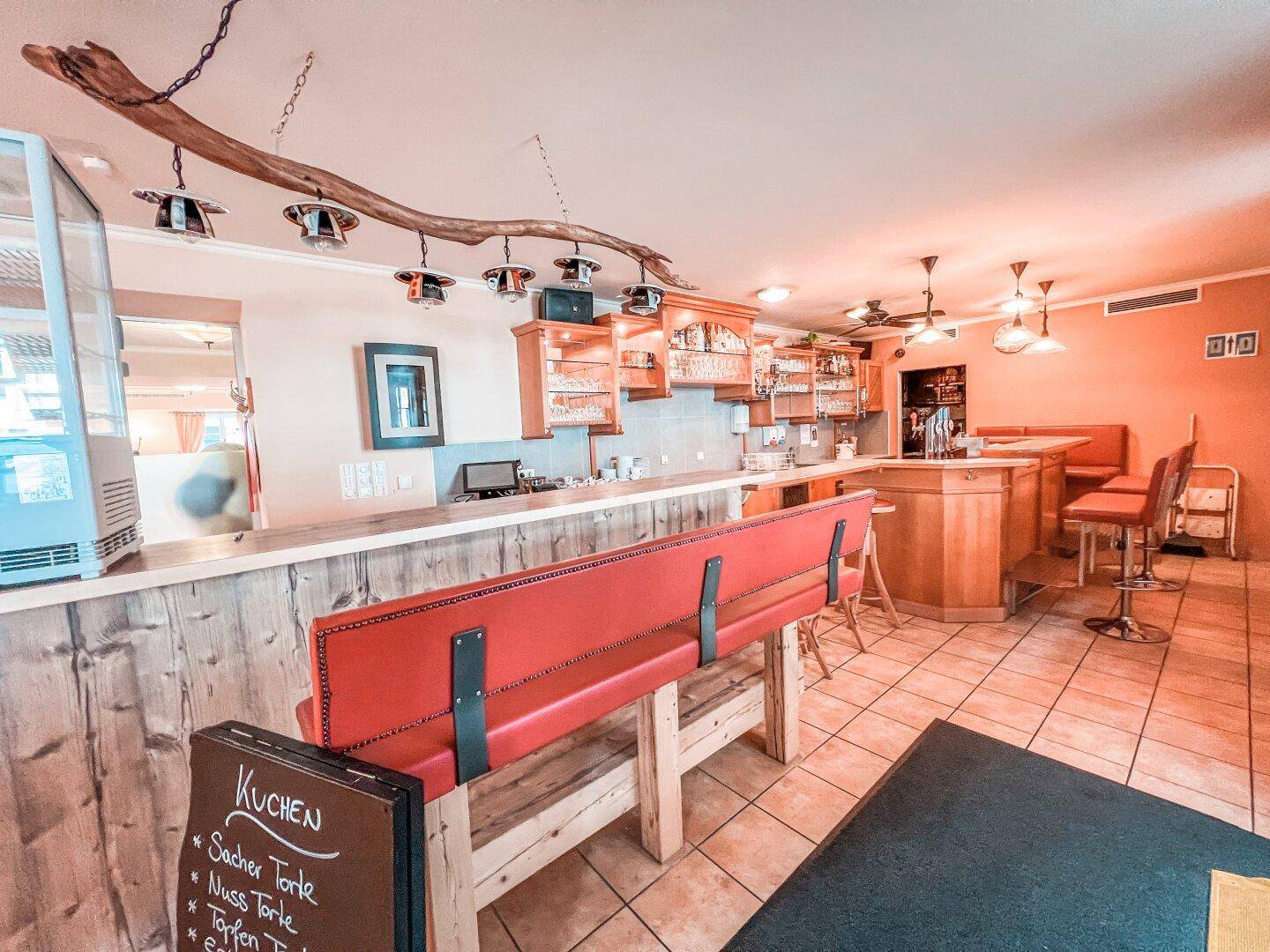 Bar- und Thekenbereich mit Holzelementen, roten Sitzbänken und Fliesenboden in einem Gastronomiebetrieb.