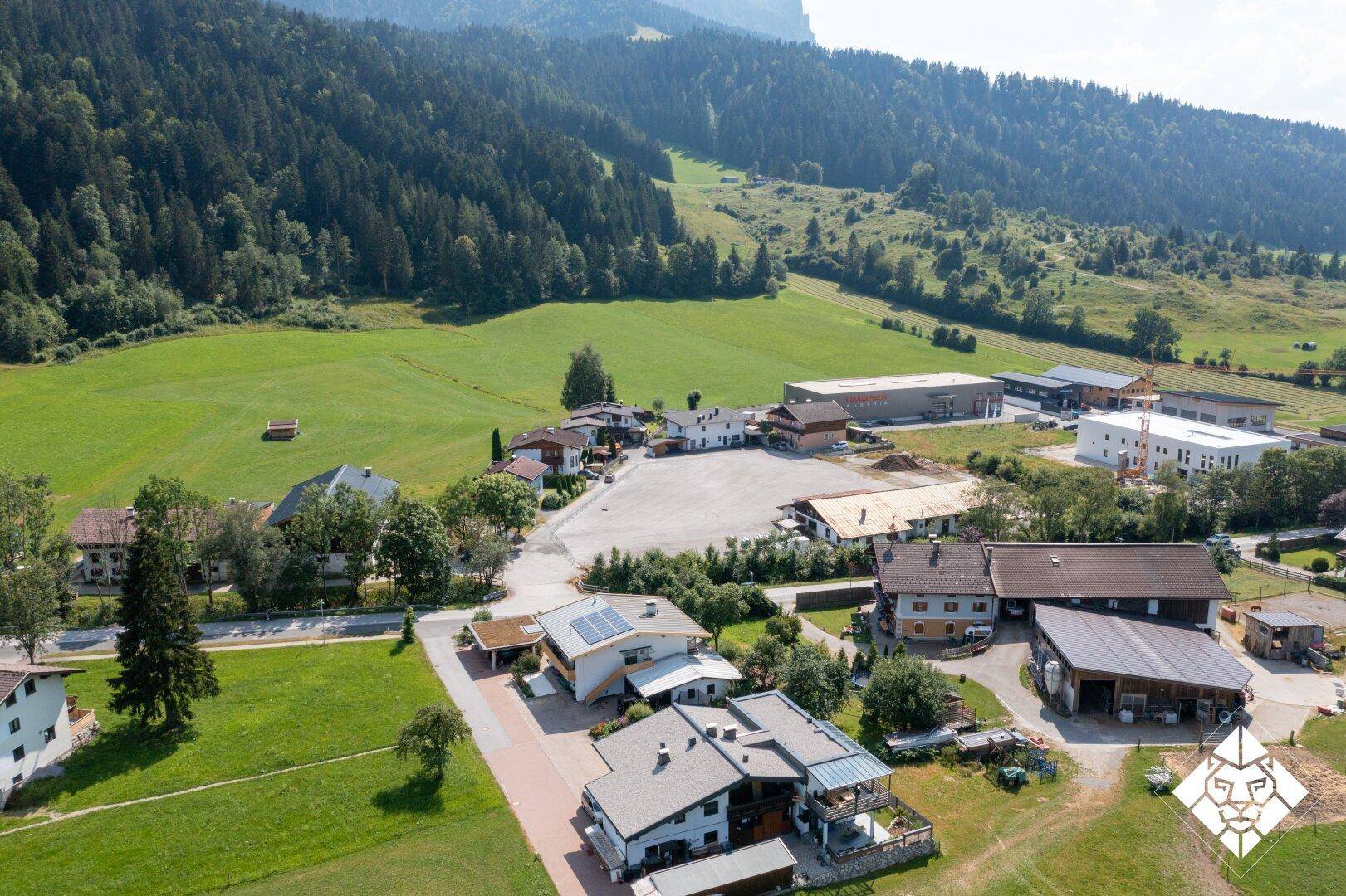 Luftaufnahme eines ländlichen Gebiets mit Wohnhäusern, grünen Wiesen und einem Wald im Hintergrund.