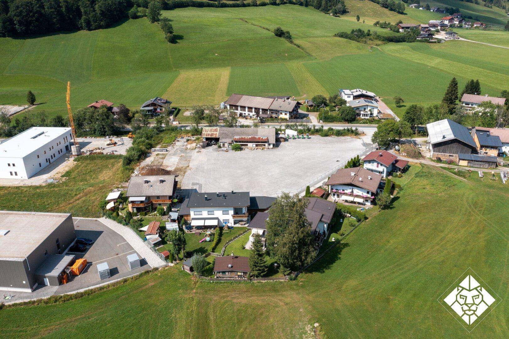 Weitläufige Luftaufnahme einer ländlichen Siedlung mit Wohnhäusern, Feldern und einer großen Freifläche.
