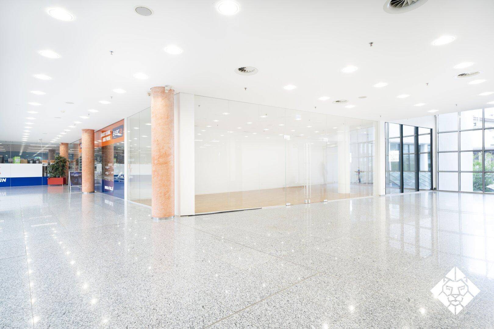 Blick auf einen modernen Ladenbereich mit Glasfront innerhalb eines Einkaufszentrums mit glänzendem Fliesenboden.
