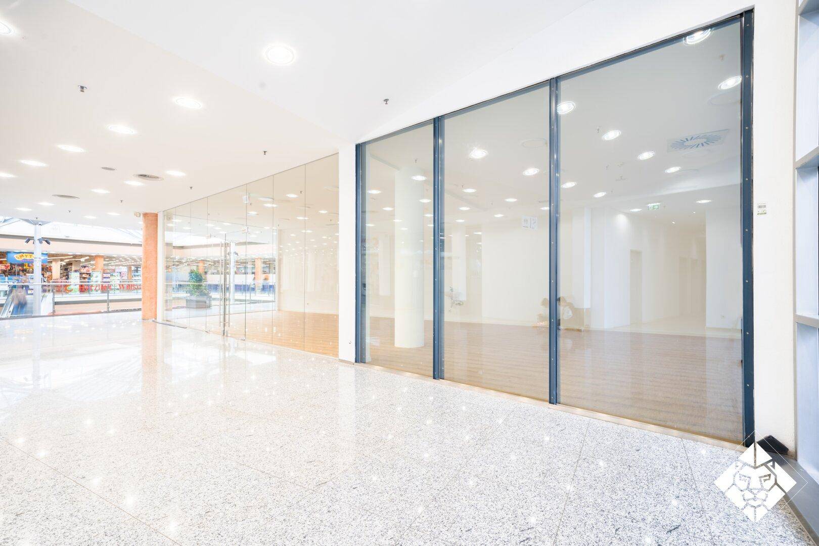 Ansicht der Glasfassade eines Ladenlokals in einem modernen Einkaufszentrum mit hellem Fliesenboden.