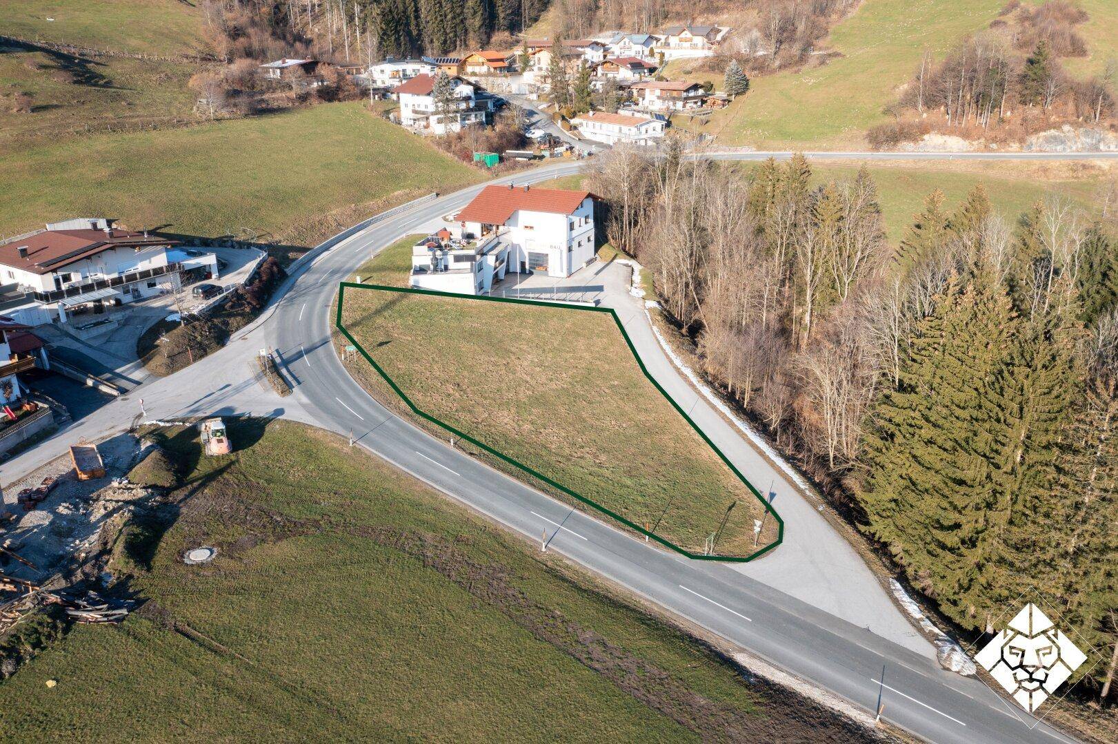 Luftaufnahme eines Baugrundstücks, umrandet von einer grünen Linie, neben einer Straße und einem Wohnhaus.