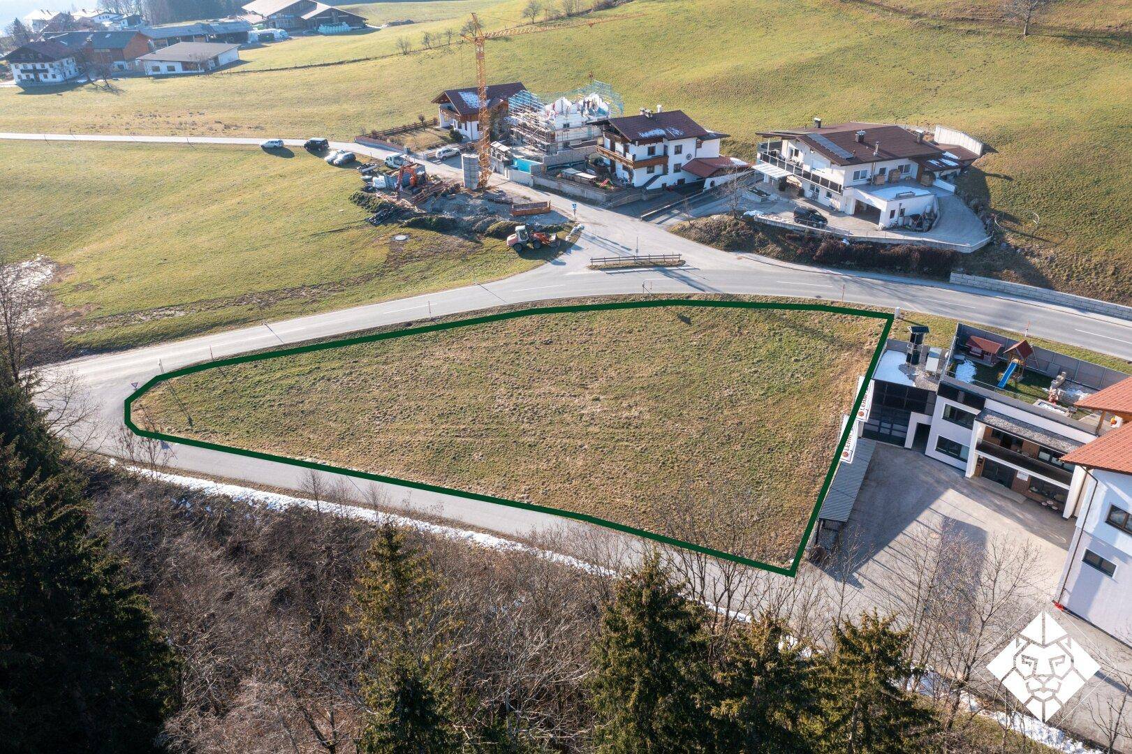 Luftaufnahme des Baugrundstücks mit grüner Markierung, angrenzend an eine Baustelle und weitere Gebäude.