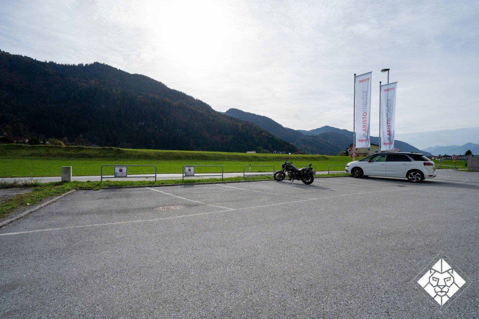 Großer Parkplatz mit einem Motorrad und einem Auto, umgeben von grünen Hügeln.
