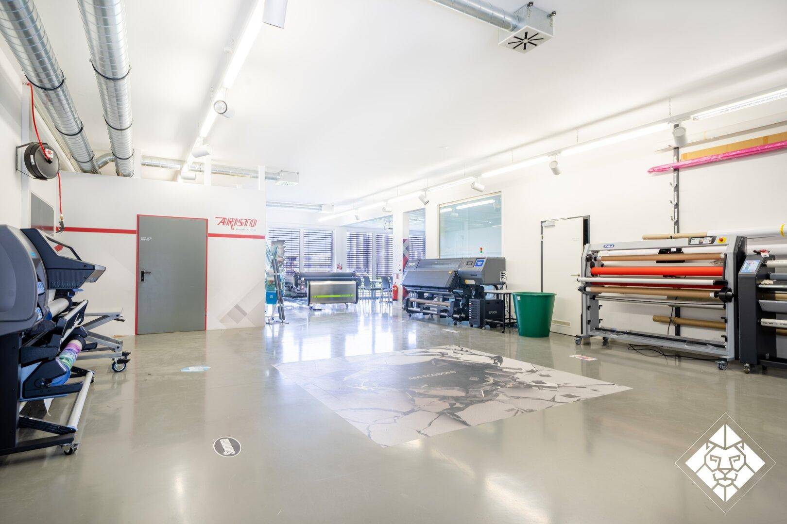 Großer Produktionsraum mit Industrieboden, Druckmaschinen und sichtbaren Lüftungsrohren.