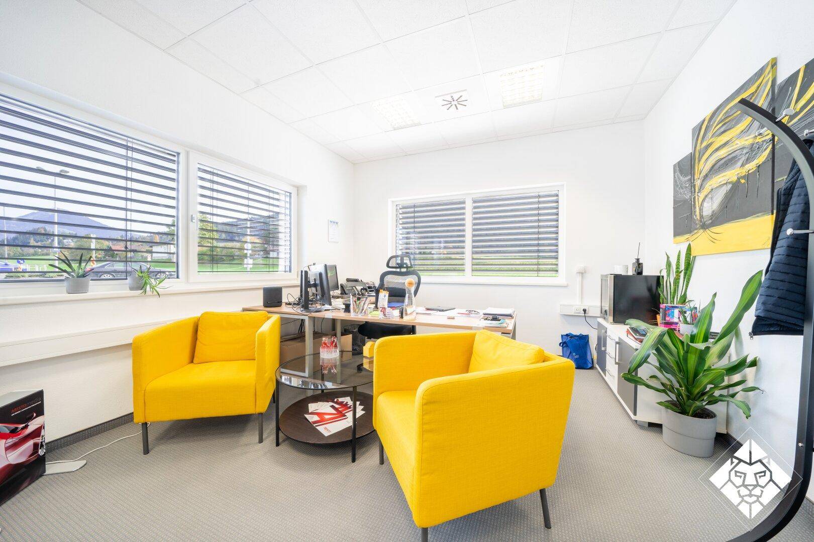 Modernes Büro mit gelben Sesseln, Schreibtisch und großen Fenstern mit Blick ins Grüne.
