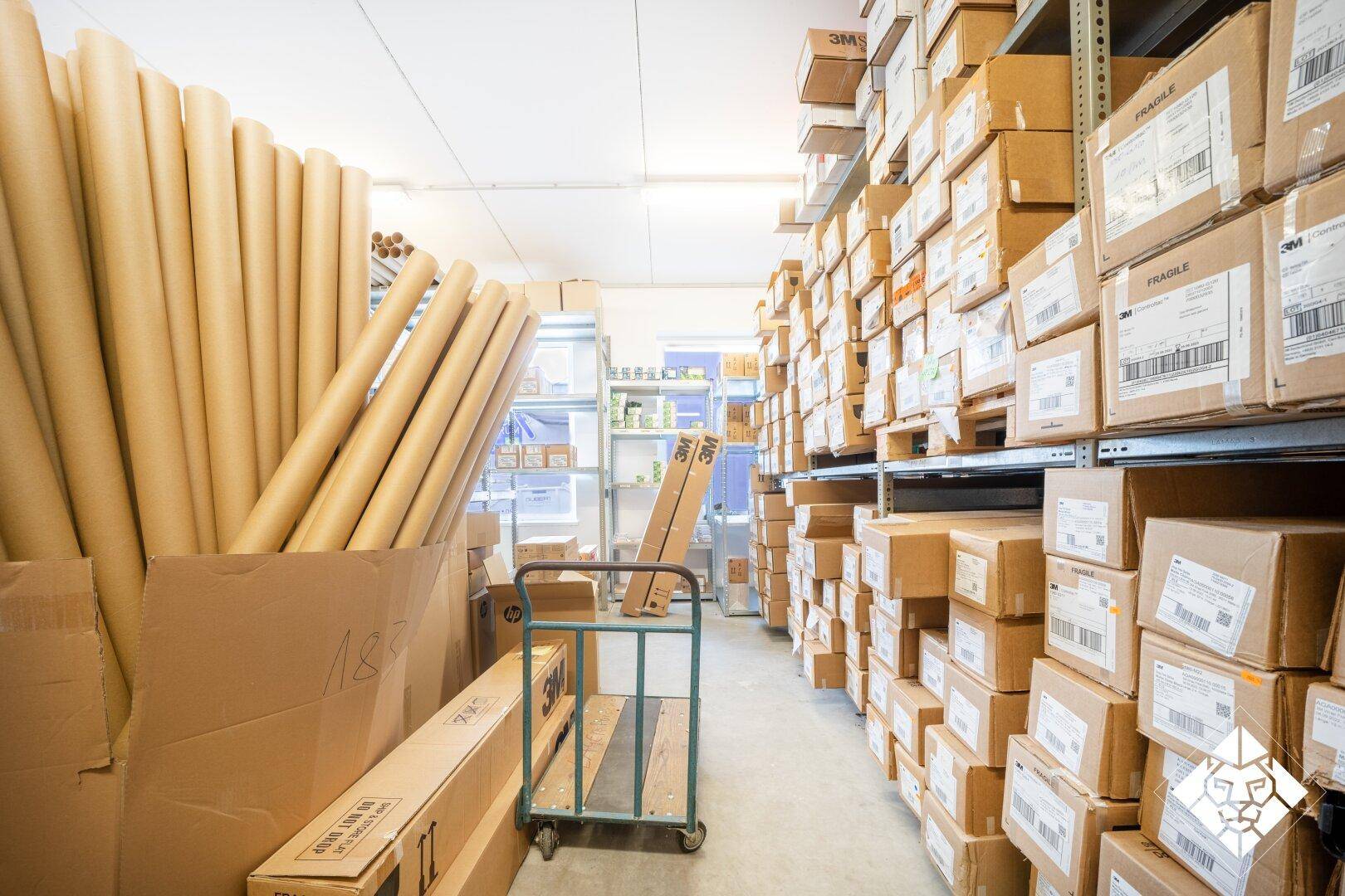 Lagerraum mit hohen Regalen, gefüllt mit Kartons und Rollen von Verpackungsmaterial.