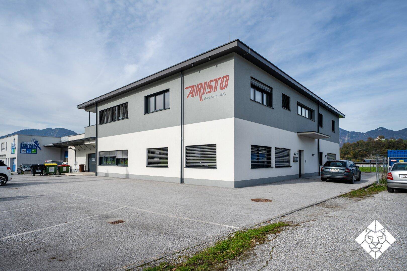 Modernes Geschäftsgebäude mit weißer und grauer Fassade sowie Parkplätzen.