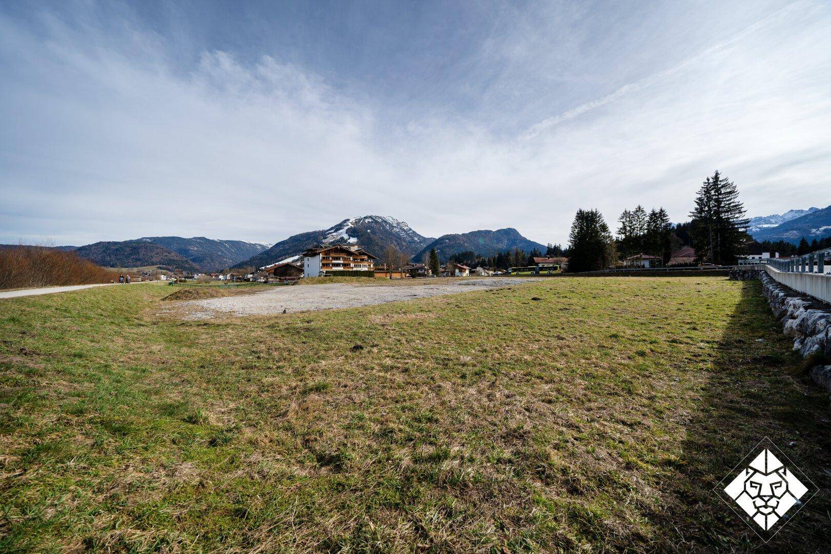 Weitläufiger Blick über das grüne Grundstück mit Bergen im Hintergrund und einem Gebäude in der Ferne.