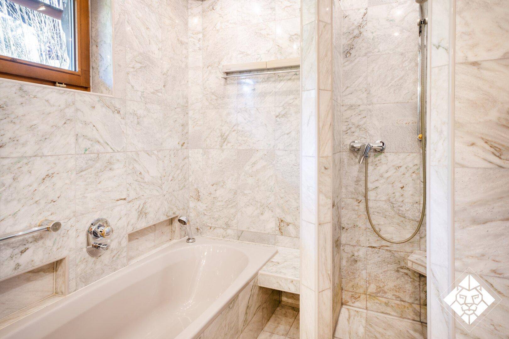 Marmoriertes Badezimmer mit Badewanne und Duschbereich, hell gefliest.