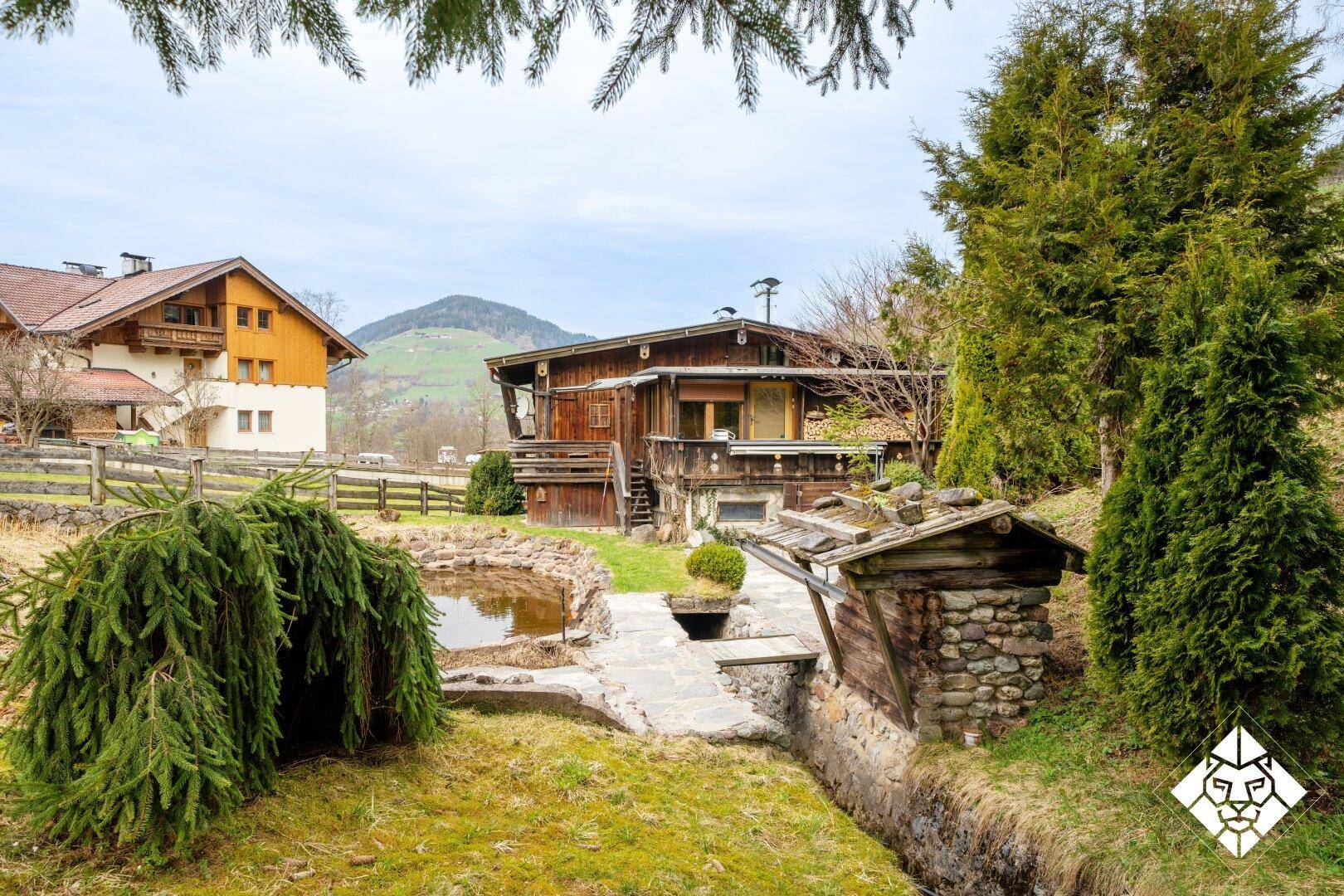 Rückansicht des Holzchalets mit Garten, Teich und Blick auf die Berge.