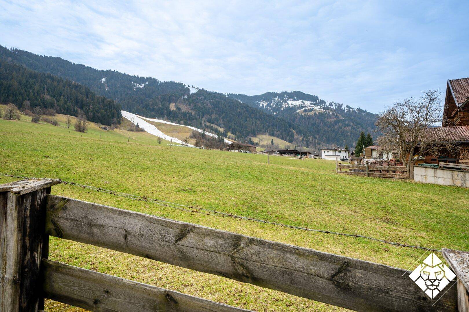 Weitläufiger Blick über grüne Wiesen und schneebedeckte Berge in der Ferne.