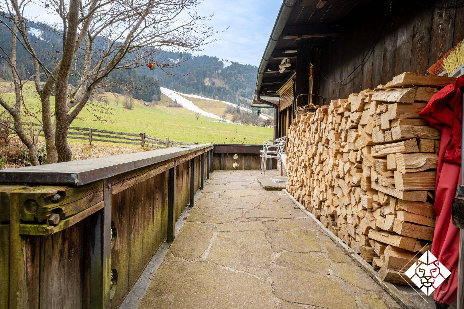 Langer Balkon mit Holzgeländer und gestapeltem Brennholz, bietet Bergblick.