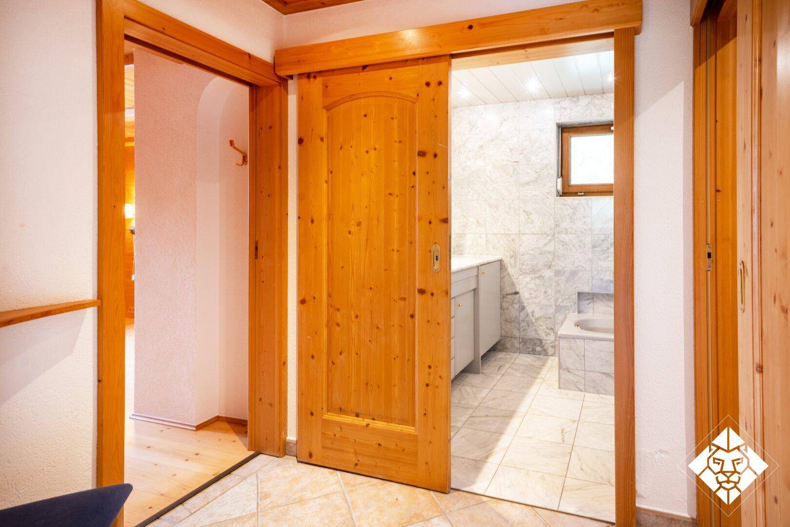 Flur mit Holztüren und Zugang zu einem gefliesten Badezimmer.