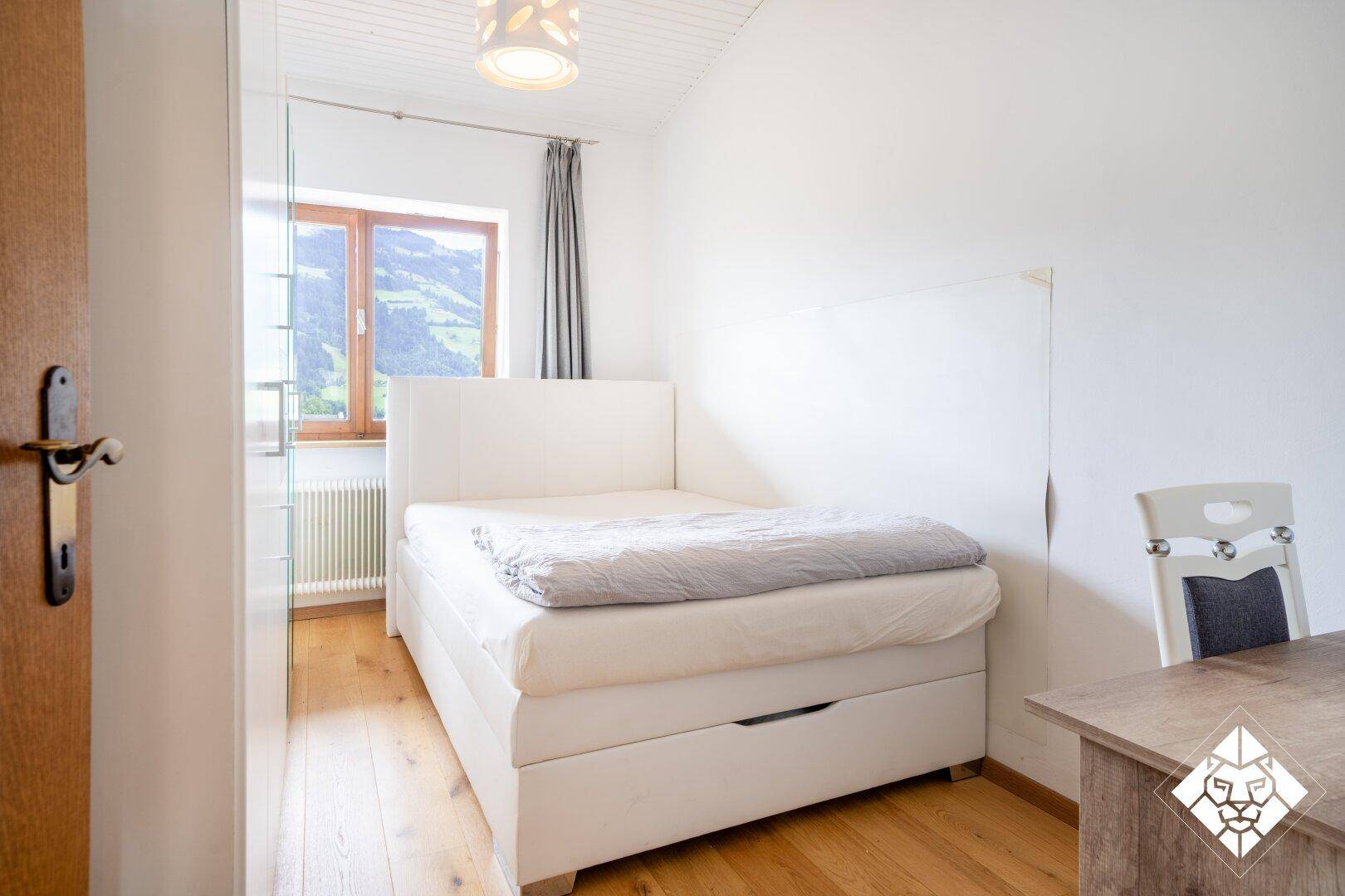 Kleines, helles Schlafzimmer mit weißem Bett, Holzboden und Fenster, schlicht und funktional.
