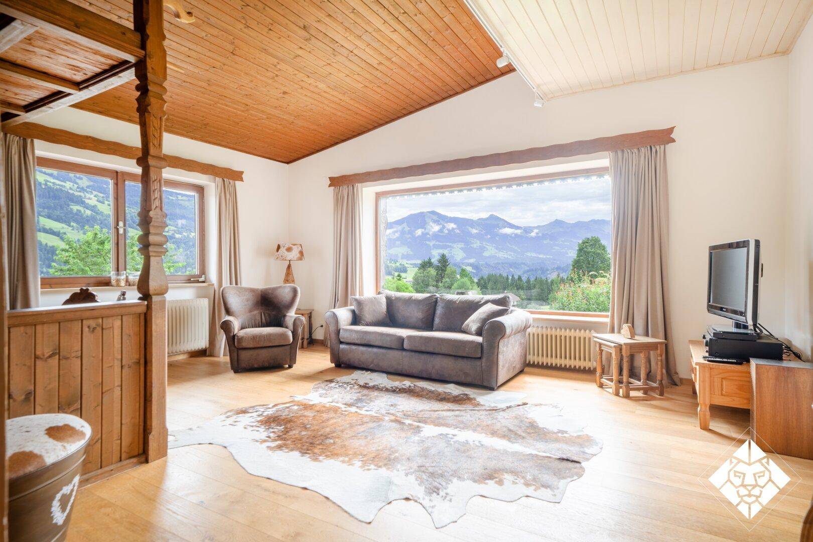 Gemütliches Wohnzimmer mit Holzboden und -decke, großem Fenster und atemberaubendem Bergblick.