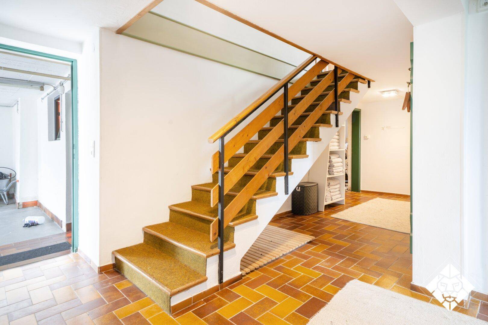 Geräumiger Eingangsbereich mit Holztreppe und Fliesenboden, führt in die oberen Etagen.