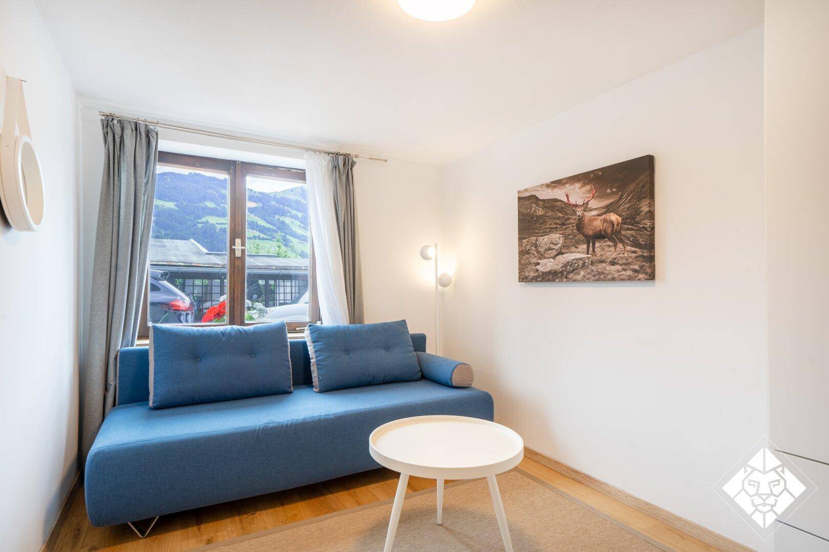 Modernes Wohnzimmer mit blauem Sofa, Holzboden und Fenster mit Blick auf die umliegenden Berge.