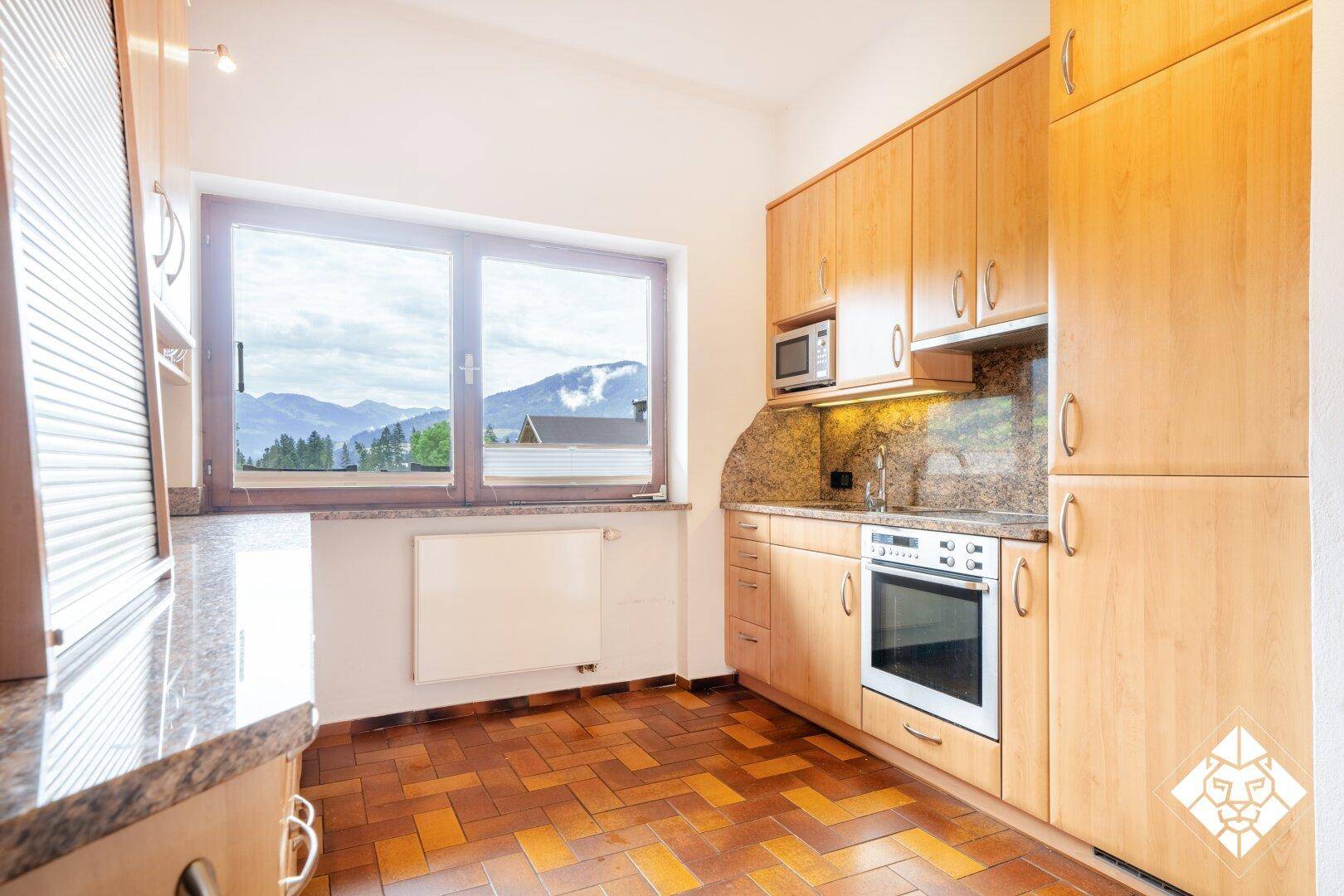 Helle Küche mit Holzschränken, Granitarbeitsplatten und Fenster mit Bergblick, ausgestattet mit Geräten.