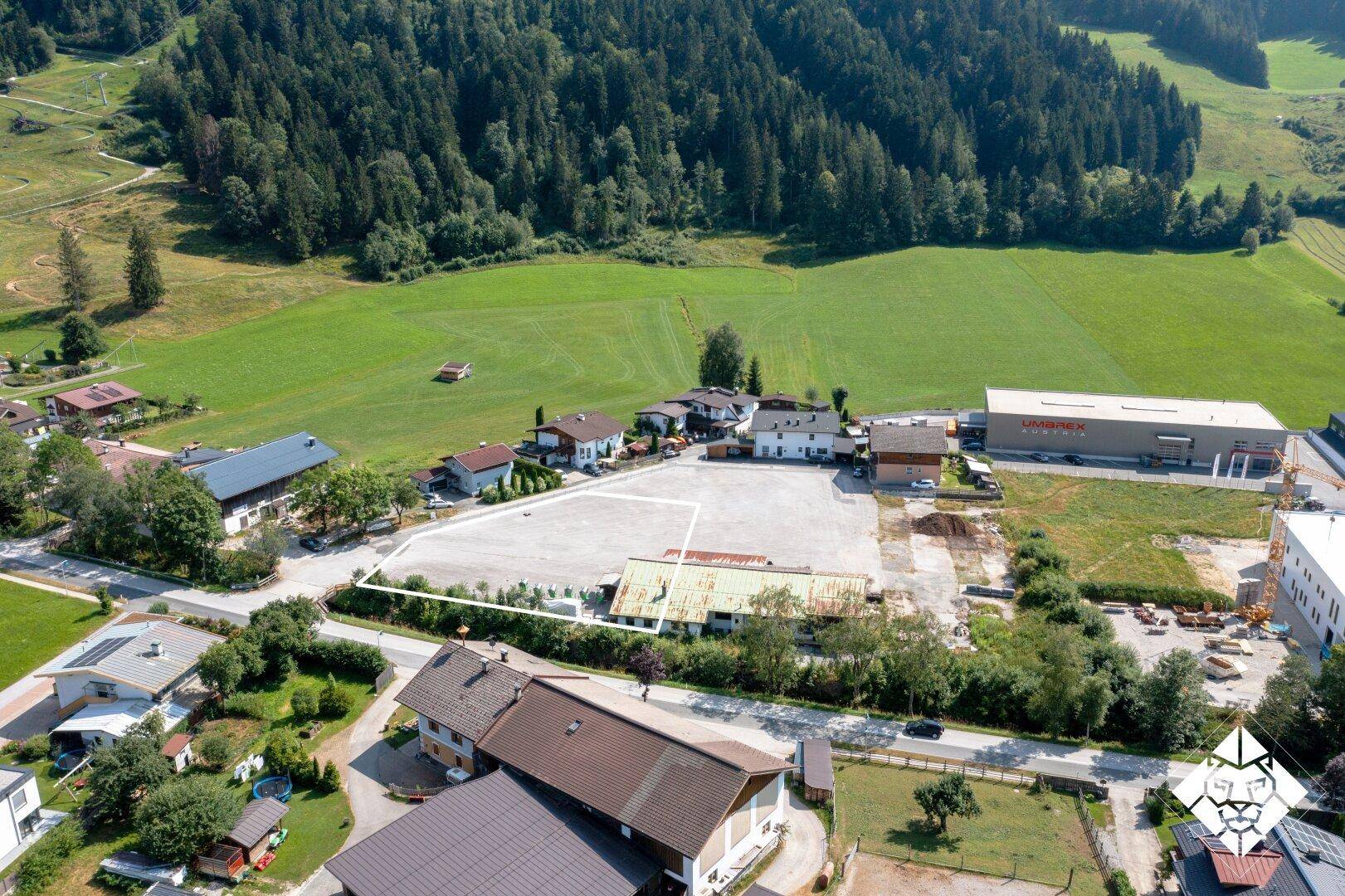 Weitläufige Luftaufnahme einer ländlichen Siedlung mit Wald, Wiesen und einem großen unbebauten Grundstück.
