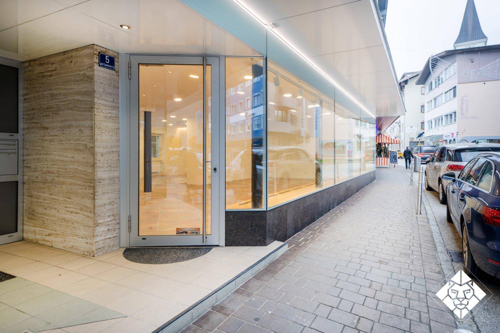 Moderne Geschäftsfassade mit großer Glasfront, Eingangstür und Natursteinverkleidung an der Straße.