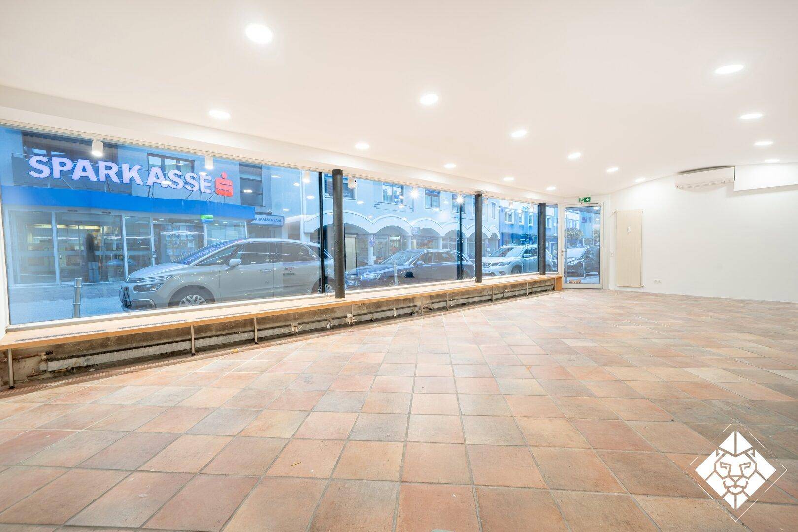 Heller Geschäftsraum mit großen Schaufenstern, Blick auf die Straße und Terrakotta-Fliesenboden.