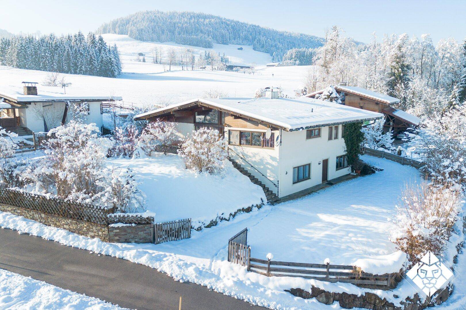 Einfamilienhaus in verschneiter Umgebung mit traditioneller Architektur und Holzelementen unter blauem Himmel.