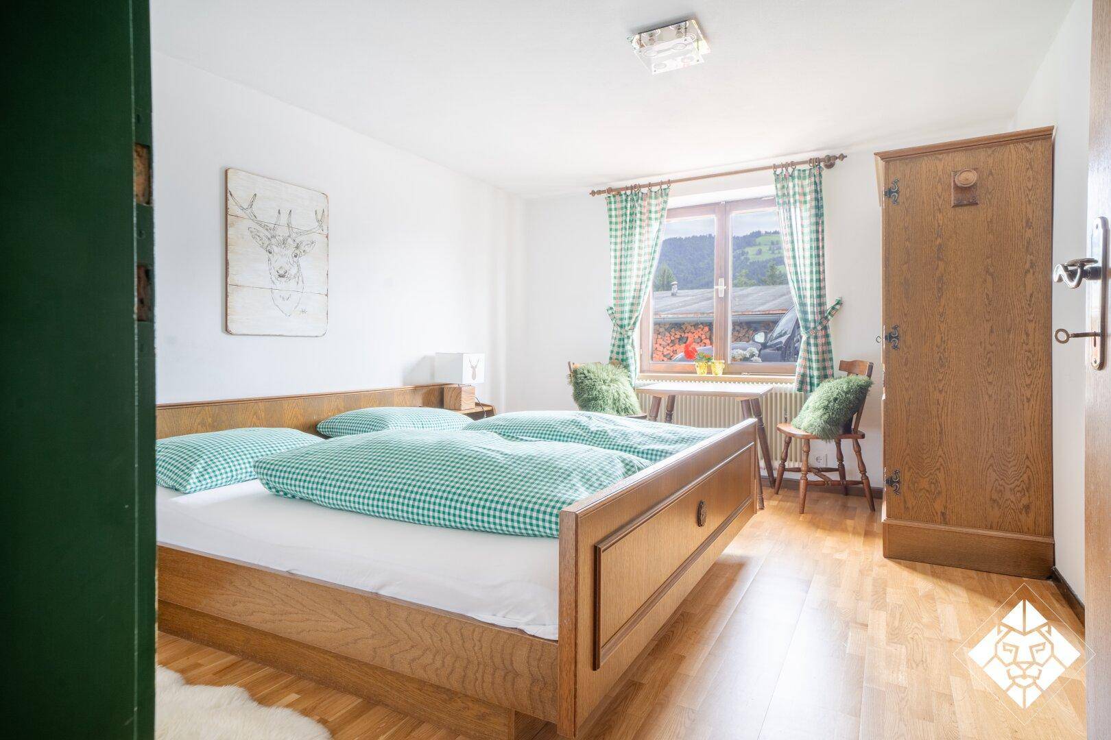 Helles Schlafzimmer mit Holzbett, Parkettboden und Fenster mit Blick ins Grüne, traditionell eingerichtet.