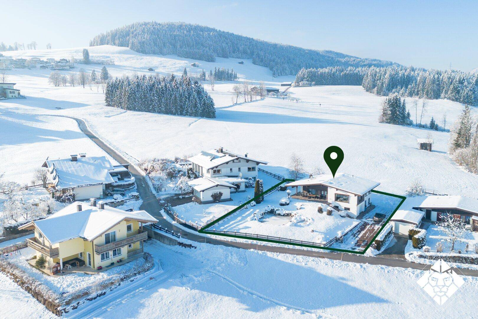 Luftaufnahme eines Hauses in verschneiter Landschaft mit markiertem Grundstück und Bergblick.