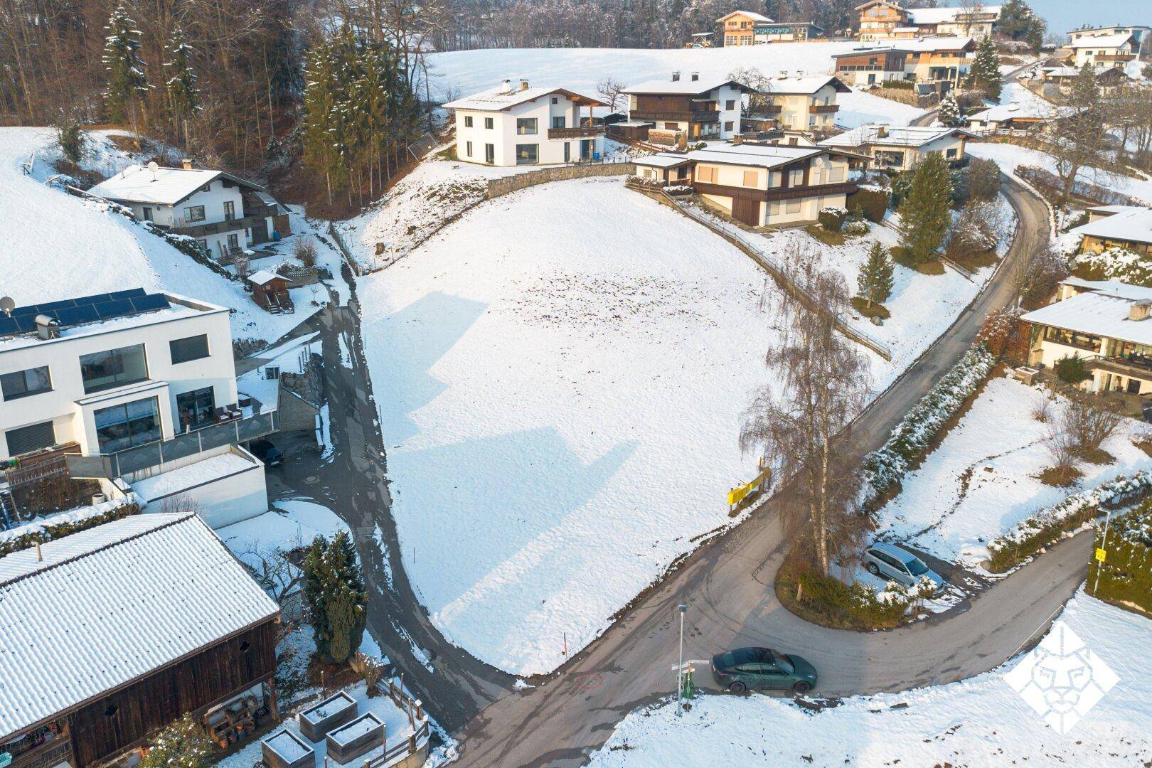 Luftaufnahme einer verschneiten Wohnsiedlung mit Häusern, Straßen und einem weiten schneebedeckten Feld.
