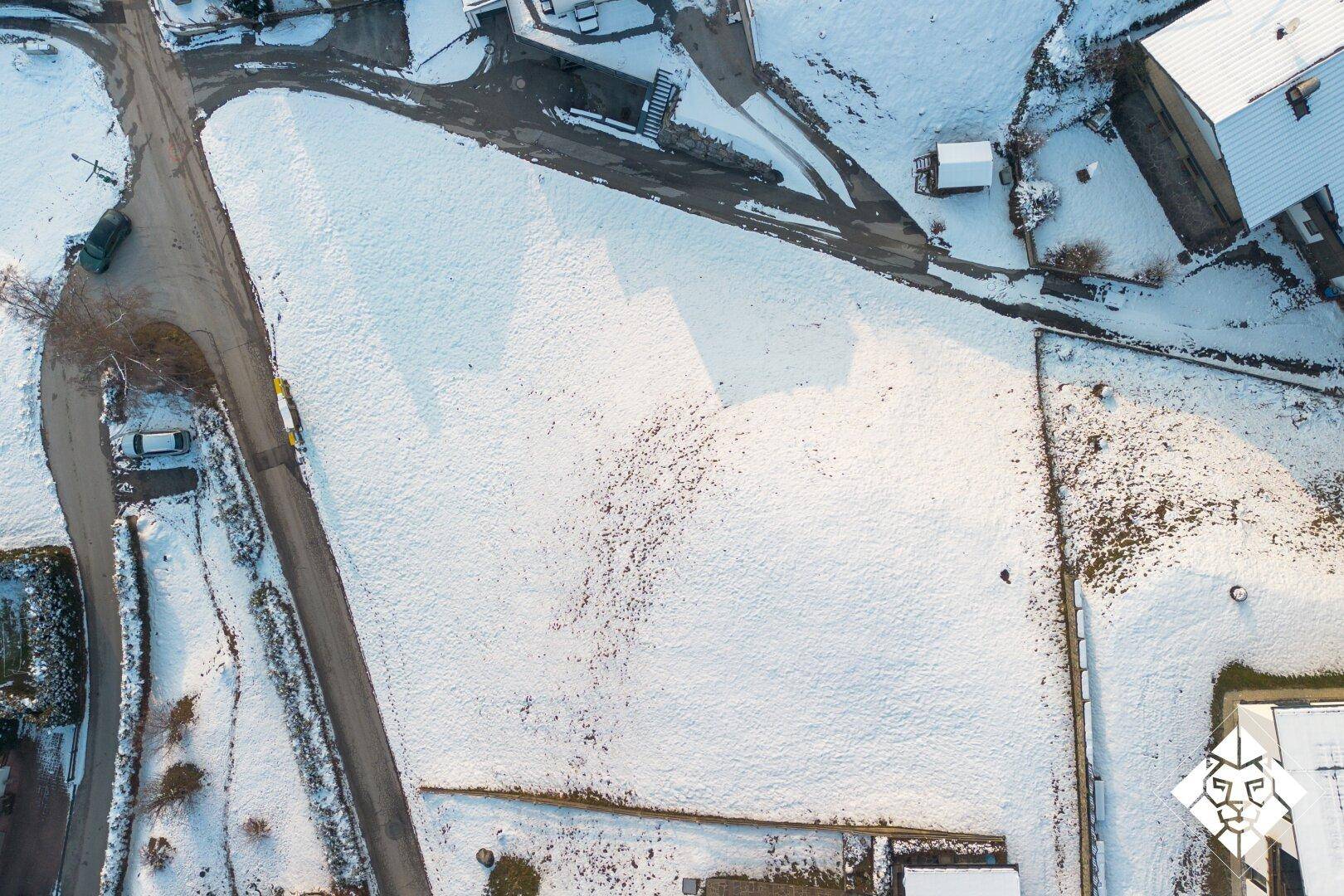 Blick von oben auf ein schneebedecktes Feld mit angrenzenden Straßen und Wohnhäusern.