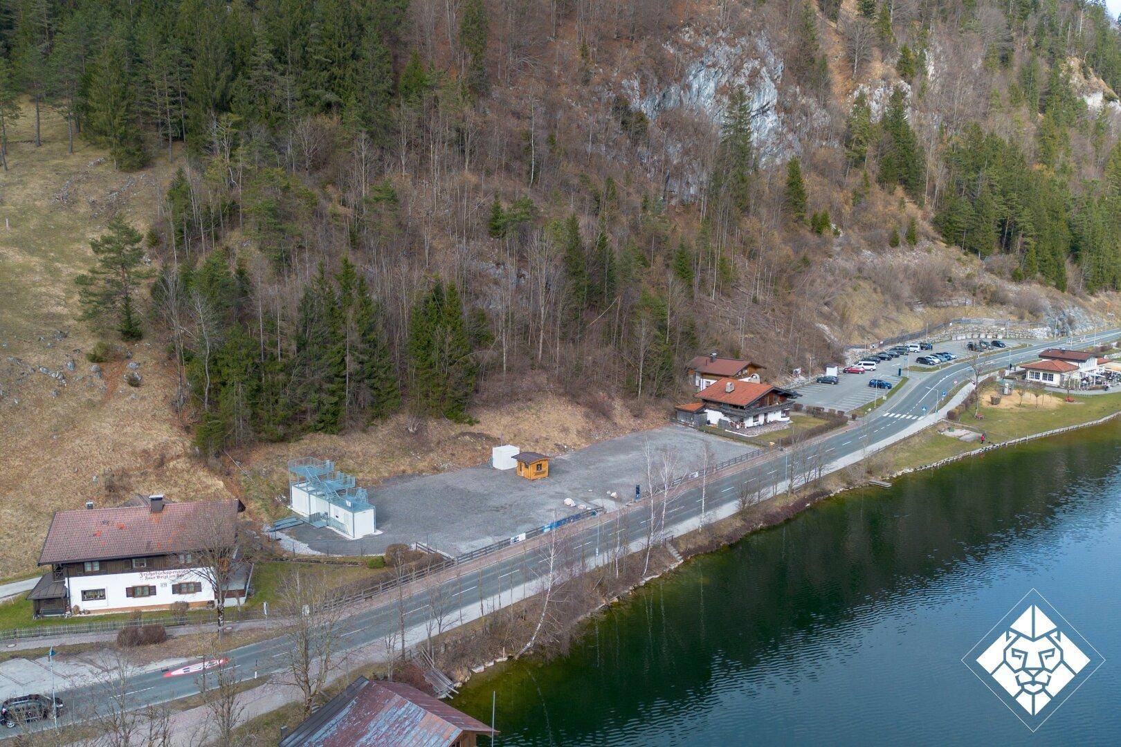 Luftaufnahme des Grundstücks mit Blick auf den See, die Straße und die angrenzenden Gebäude.