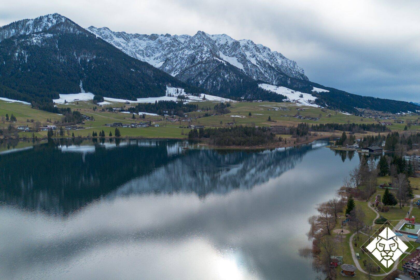 Weitläufige Luftaufnahme eines Sees, der die umliegenden Berge und den Himmel widerspiegelt.