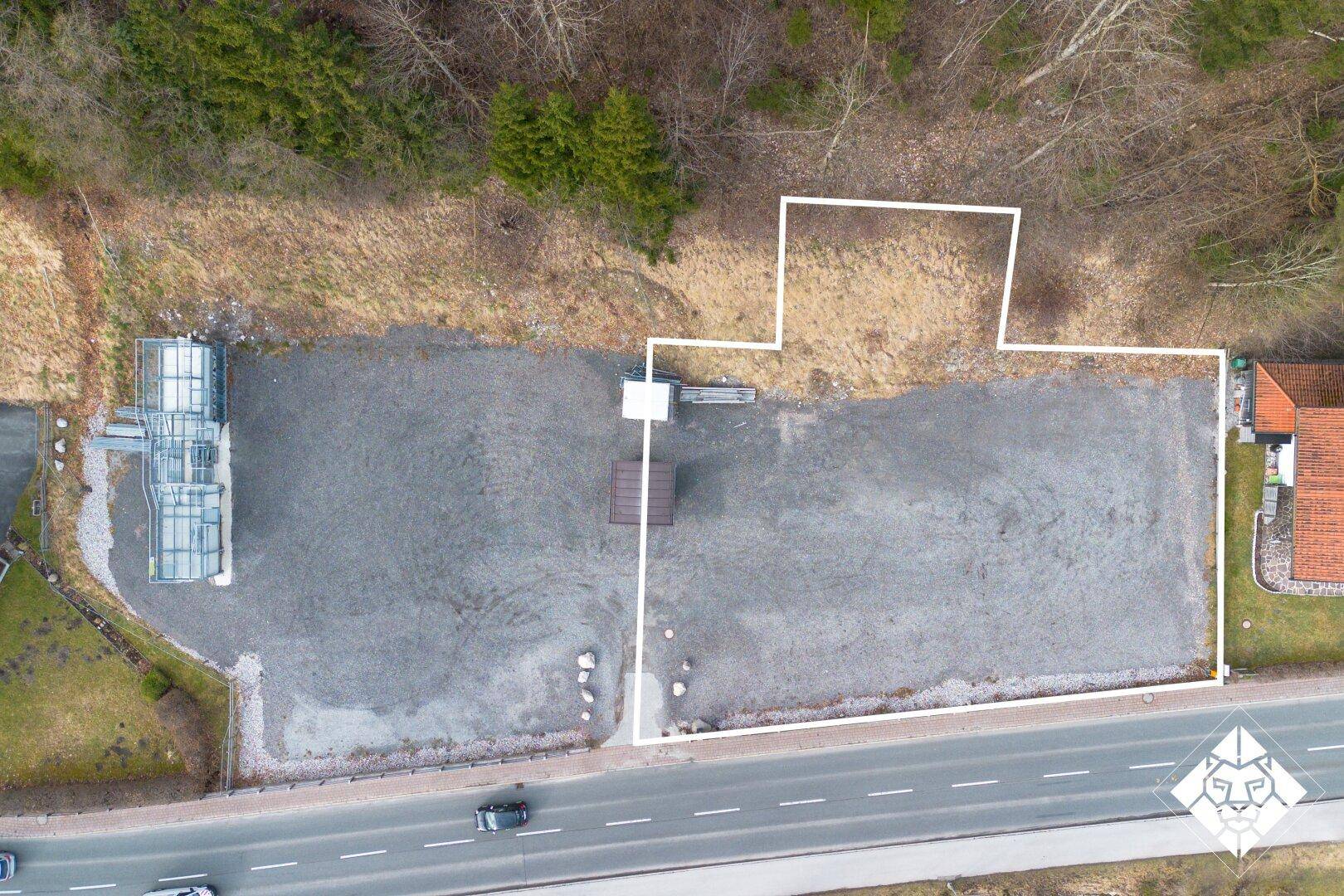 Draufsicht auf ein großes Schottergrundstück neben einer Straße, umgeben von Wald und Natur.