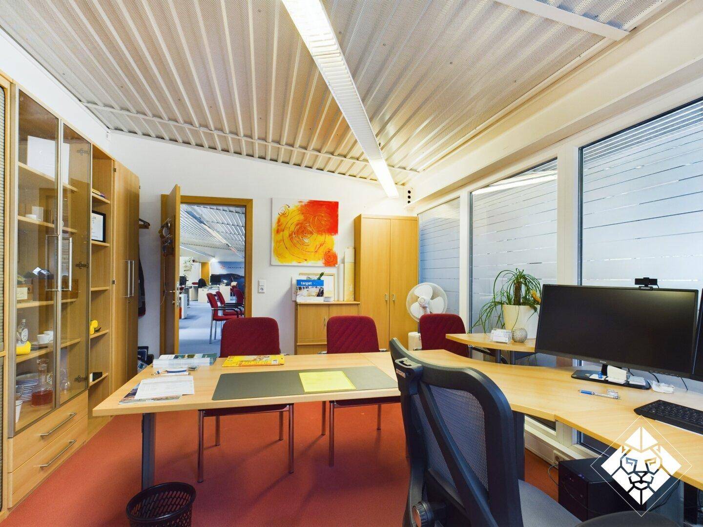 Büro mit rotem Teppichboden, Holzmöbeln und einem Schreibtisch, der den Blick auf den Flur freigibt.