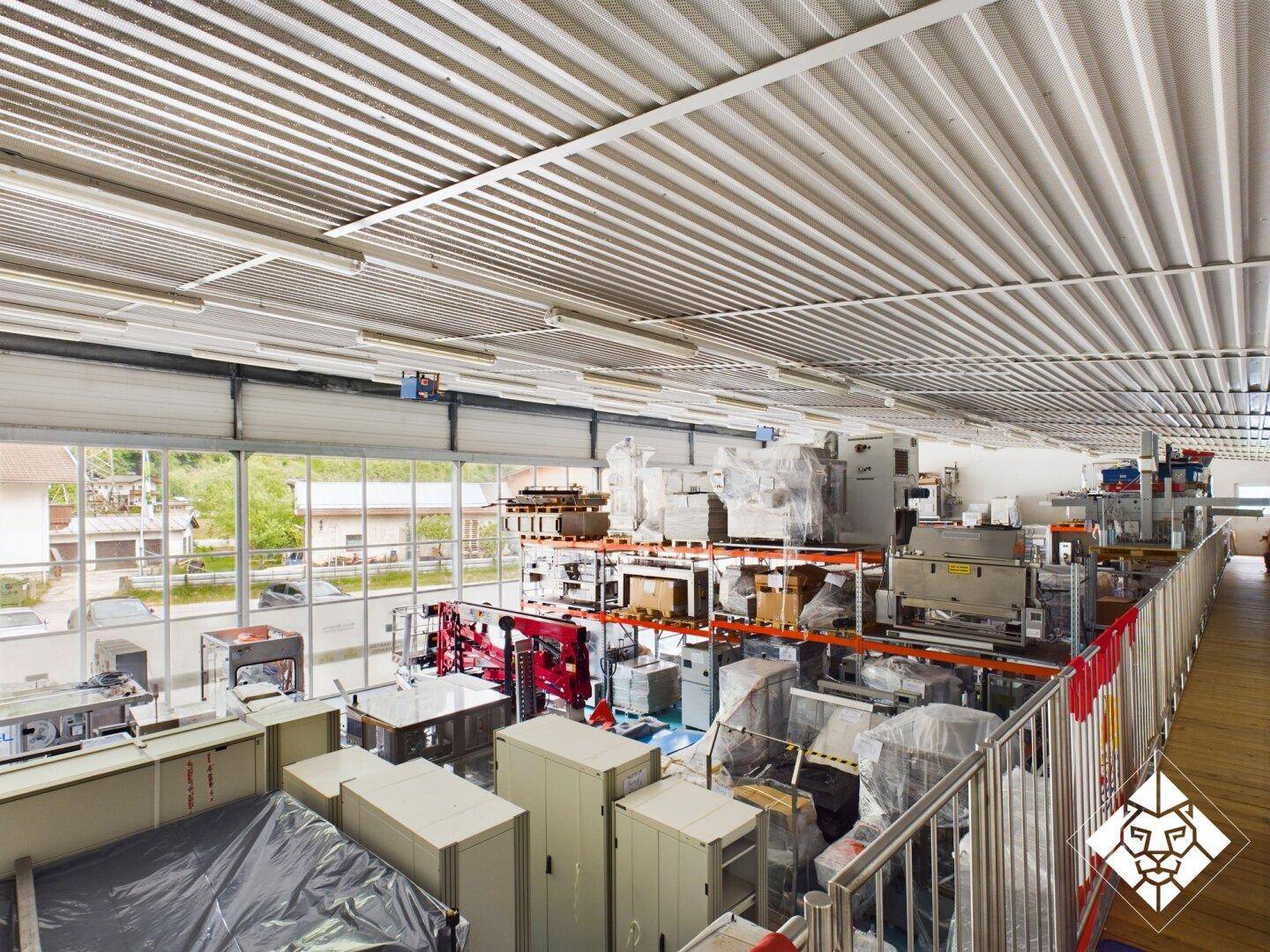 Große Produktionshalle mit Maschinen, Lagerregalen und hohen Decken, gut beleuchtet.