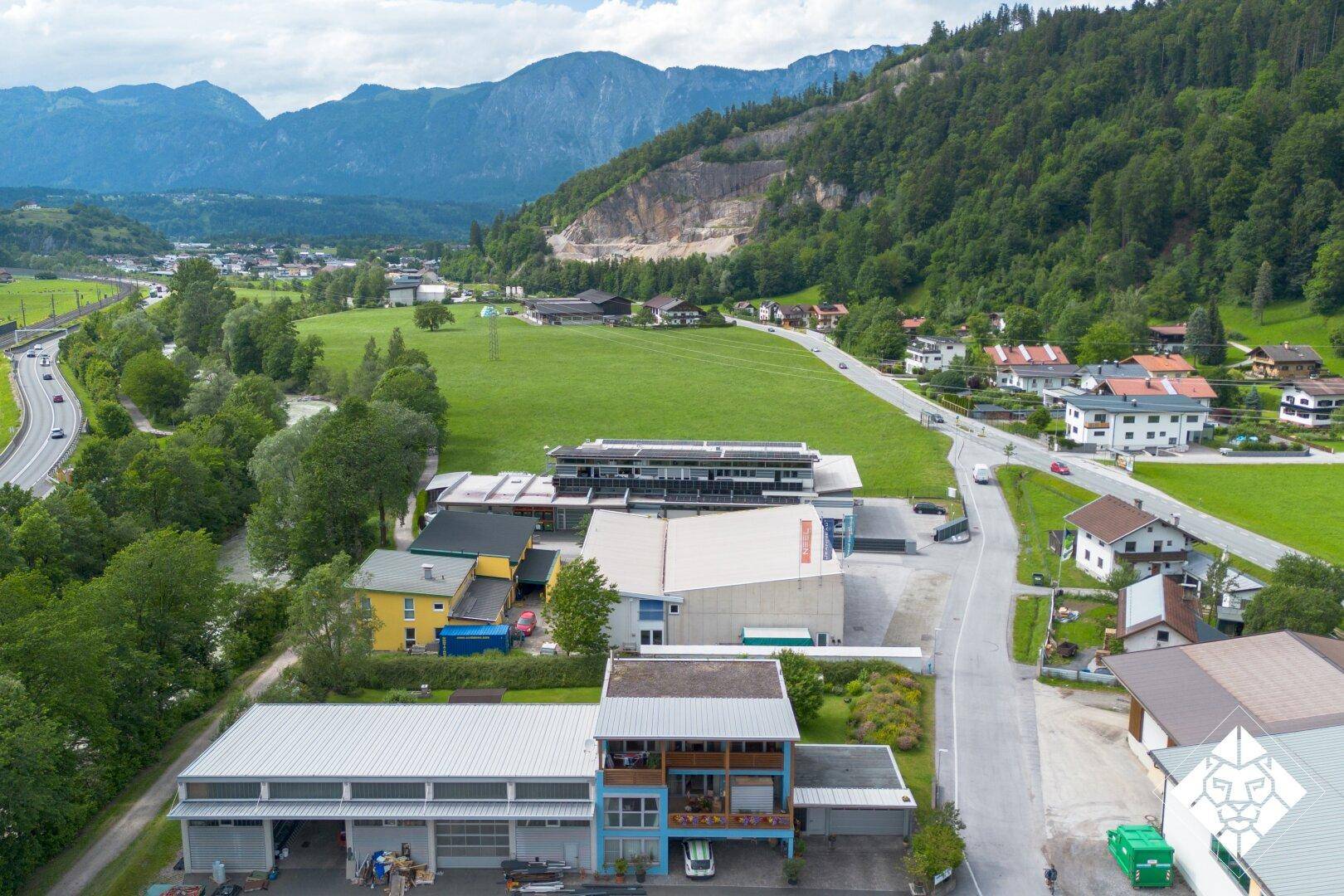 Weitläufige Luftaufnahme eines Gewerbegebiets und Wohnsiedlung umgeben von grünen Bergen und Tälern.