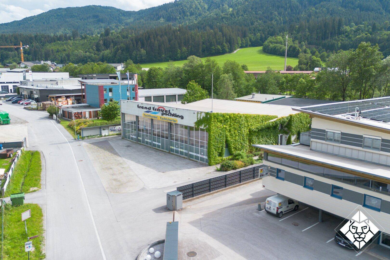 Luftaufnahme eines Gewerbegebäudes mit begrüntem Dach und angrenzenden Parkplätzen in ländlicher Umgebung.