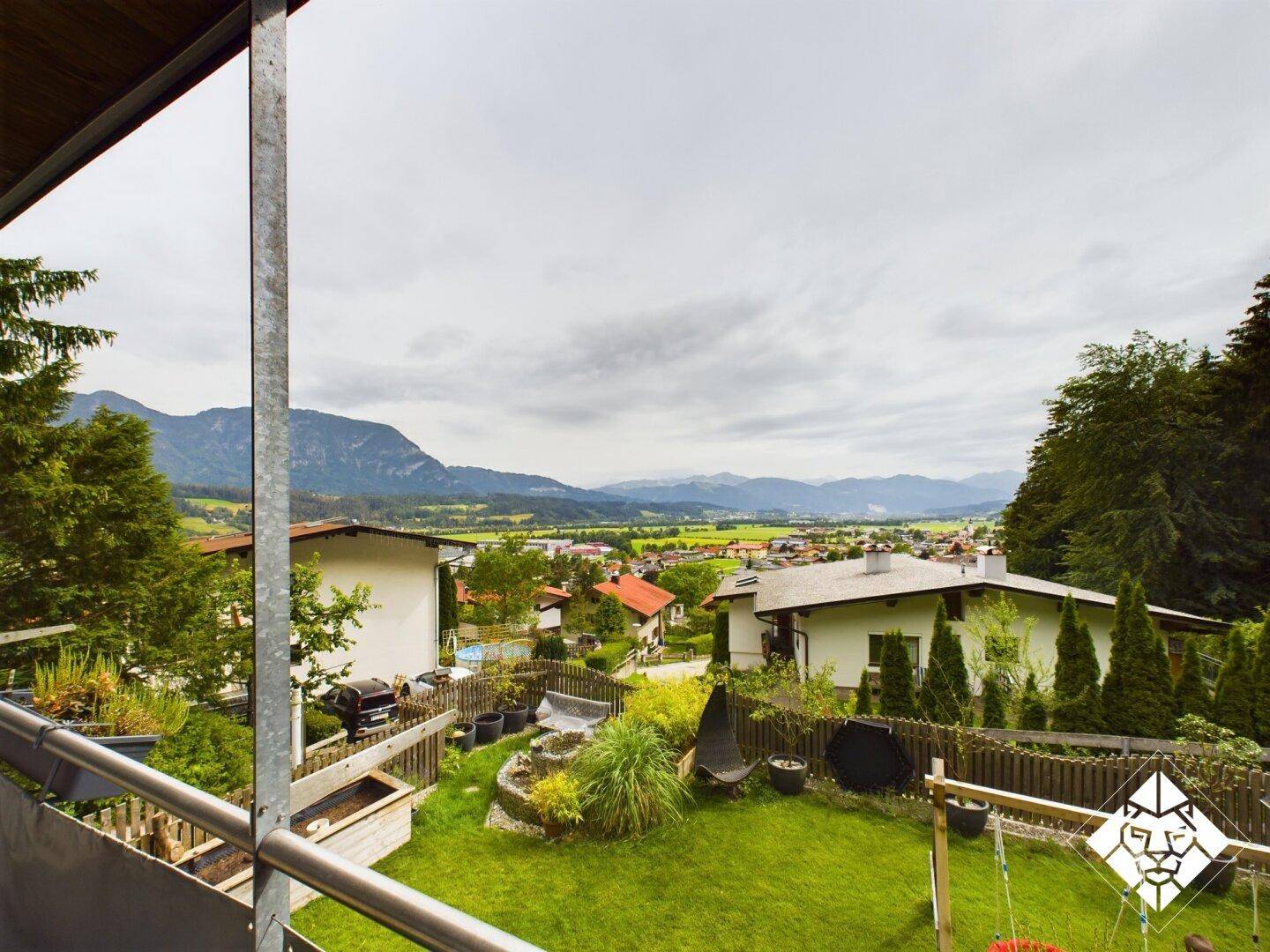 Weitläufiger Blick vom Balkon auf die grüne Landschaft, Berge und umliegende Häuser.