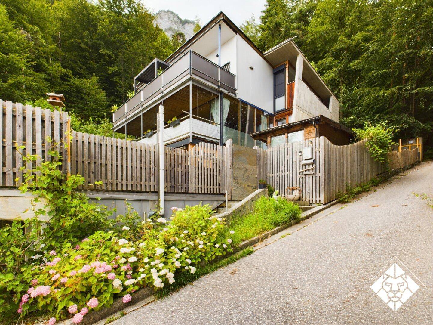 Modernes Haus in Hanglage mit mehreren Balkonen und üppiger Vegetation.
