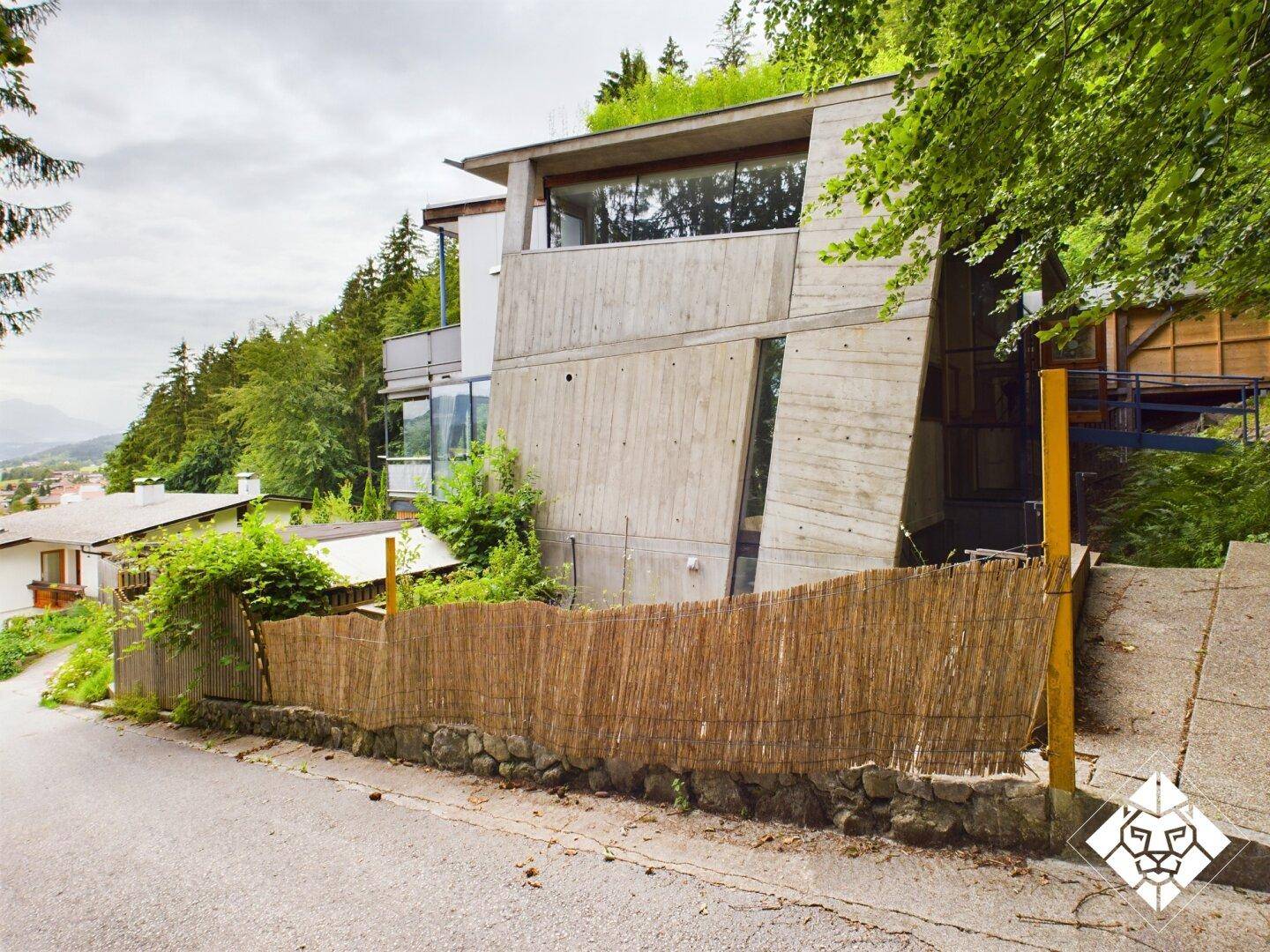 Architektonisch interessantes Gebäude mit Betonfassade und integriertem Gründach in bewaldeter Umgebung.