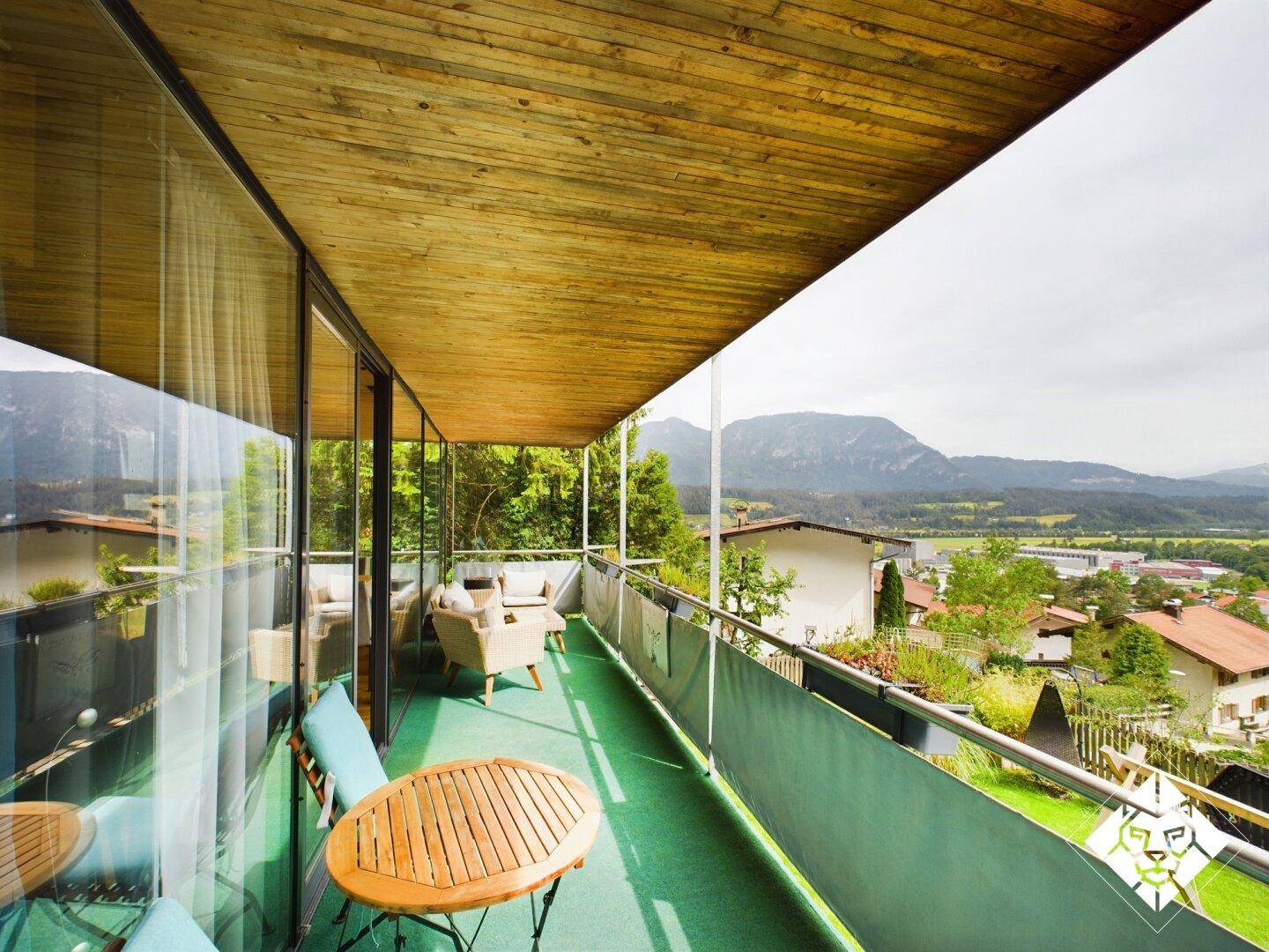 Langer Balkon mit Sitzgelegenheiten, Holzboden und weitem Blick auf die Berge und das Tal.