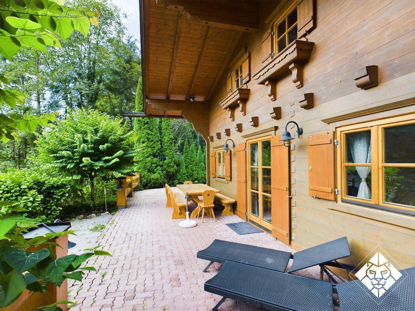 Gemütliche Terrasse mit Sonnenliegen und Esstisch vor dem Holzhaus, umgeben von viel Grün.